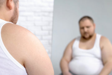 Insecure fat man sitting in front of the mirror